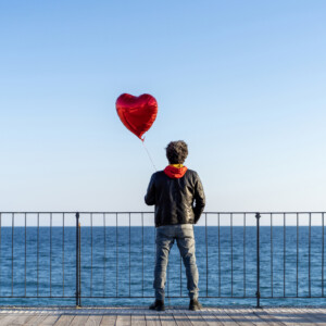 Lonely man holding a red heart shape balloon on the beach Lonely man holding a red heart shape balloon on the beach