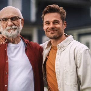 Porträt eines glücklichen älteren Vaters oder Großelternteils, der zusammen mit seinem hübschen erwachsenen Sohn posiert. Familienmitglieder umarmen einander, stehend, Blick auf die Kamera und lächelnd. Porträt eines glücklichen älteren Vaters oder Großelternteils, der zusammen mit seinem hübschen erwachsenen Sohn posiert. Familienmitglieder umarmen einander, stehend, Blick auf die Kamera und lächelnd.