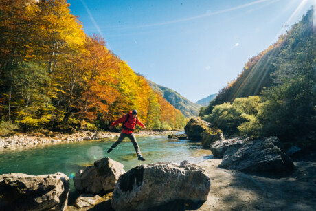 m&auml;nnliche Person springt &uuml;ber einen Flu&szlig; im herbstlichen Hochgebirge