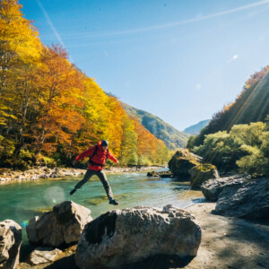 m&auml;nnliche Person springt &uuml;ber einen Flu&szlig; im herbstlichen Hochgebirge